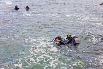 group of divers in special suits teach beginner to dive into the sea