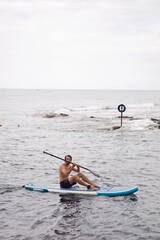 man with a beard swims on stand up paddle board on quiet blue ocean. Sup surfing in water