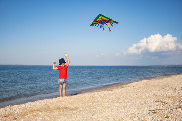 boy in a red T-shirt and striped swimming trunks launches kite on the beach by the sea in the summer on vacation