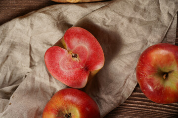 Several whole and cut apples and apple halves with red flesh on a linen cloth on a wooden table