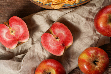 Several whole and cut apples and apple halves with red flesh on a linen cloth on a wooden table