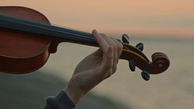 Young musician is playing violin, bowing along the strings skillfully, standing on lakeshore in the morning, inspired by sunrise, Detailed plan, Slow motion.