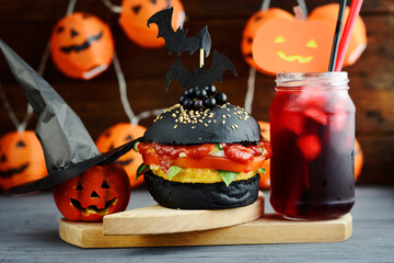 Halloween Spooky Black Burger. Cheeseburger on Halloween pumpkin head jack lantern holiday food background	
