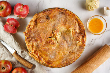 Classic traditional cinnamon apple pie and red flesh apples on a marble table, top view