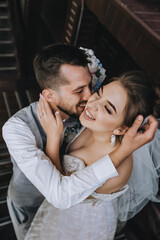 Close-up wedding portrait of beautiful, cheerful and happy newlyweds. Stylish smiling bearded groom in a gray waistcoat hugs a young bride.