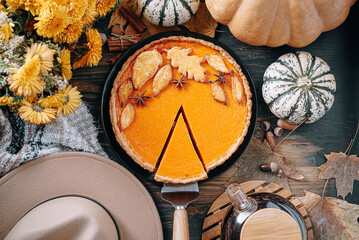 autumn composition with pumpkins, yellow tea flowers, warm plaid and hat and pumpkin pie in the center of the frame