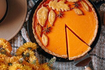 autumn composition with pumpkins, yellow tea flowers, warm plaid and hat and pumpkin pie in the center of the frame