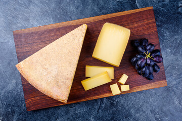 Modern style traditional aged mountain cheese of the Alps offered with grapes on a wooden design...