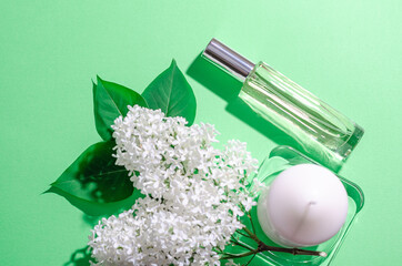 White lilac flowers, white candle and a glass bottle with perfume on a green background. Bright shadows and light. Place for your text. Flat lay. SPA and aromatherapy.