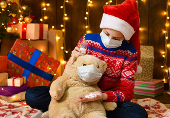 Child girl as Santa helper posing in new year decoration. Wearing a protective face mask against...
