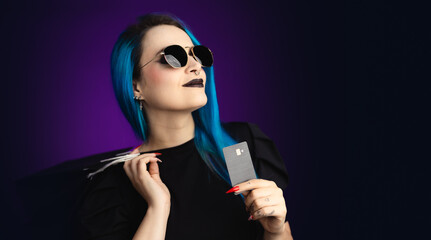 Large banner Woman in black friday, shopping, expressions with sunglasses, shopping bag and credit card in hand, blue hair, copy space, black background, neon style for websites, billboards and boards