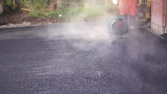 R&uuml;ttelplatte und Walze verdichten den Boden der in die Einfahrt asphaltiert wurde. 4K
