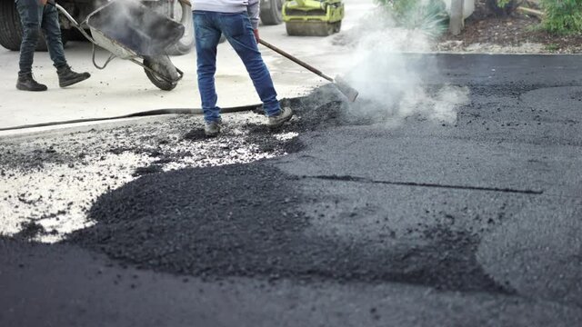 Arbeiter mit der Schaufel und dem Rechen asphaltiert die Stra&szlig;e neben der Asphaltiermaschine 4K
