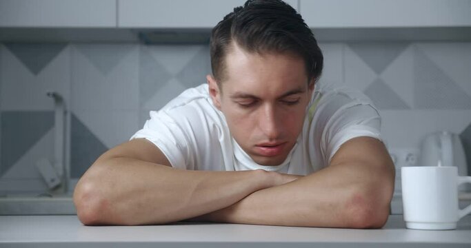 Portrait of worried and stressed young man sitting at table at home. Depressed male suffering from grief or failure