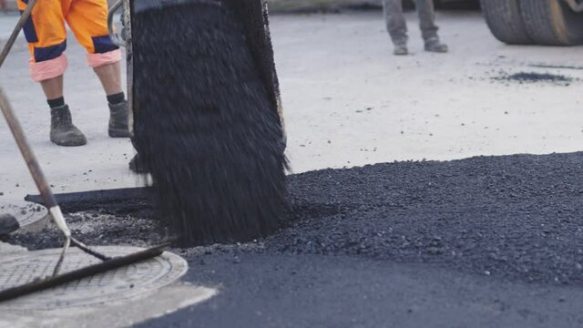 Hei&szlig;er Asphalt wird mit den Schubkarren und der Asphaltiermaschine an die richtige Stelle gekippt.