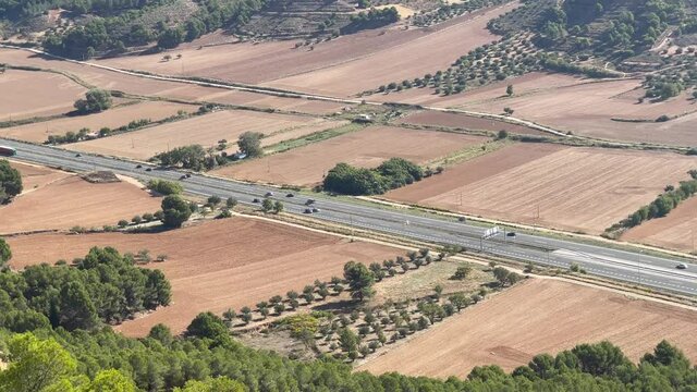 panoramic aerial view of the national highway  NII as it passes through the city of Guadalajara Spain, with cars and trucks driving along it, crop fields sown on the sides, Madrid  on the horizon