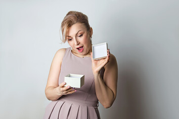 Naklejka premium On a gray background, a young woman is holding a gift and is happily surprised and happy.A gift for a woman for a holiday. A gift for mom, wife,boss.