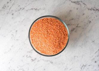 High angle view of red lentils in glass bowl on grey marbled effect background (selective focus)