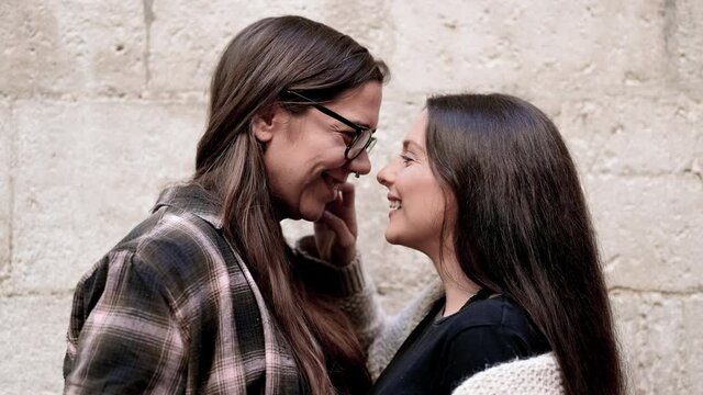 Portrait of an affectionate young lesbian couple hugging each other while standing together in front of a stone wall outside. High quality 4k footage