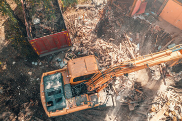 Process of demolition building dismantling aerial top view. Excavator breaking house.