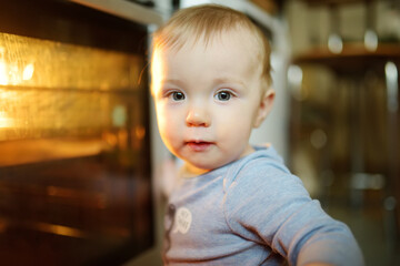 Little child playing with electric stove in the kitchen. Toddler boy near hot oven.