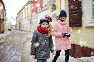 Two adorable young sisters having fun on beautiful winter day in a city. Cute children having a walk in winter town.