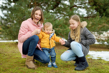 Fototapeta premium Two big sisters and their baby brother having fun outdoors. Two young girls holding their baby boy sibling on winter day. Kids with large age gap.