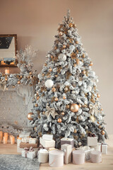 Hall room interior with a fireplace with candles and a decorated Christmas tree with presents. Large designer snow tree with lights and balls in beige, gold and silver colors 