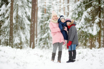 Fototapeta na wymiar Two big sisters and their baby brother having fun outdoors. Two young girls holding their baby boy sibling on winter day. Kids with large age gap.