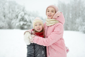 Two young girls having fun together in beautiful winter park. Cute sisters playing in a snow. Winter activities for family with kids.