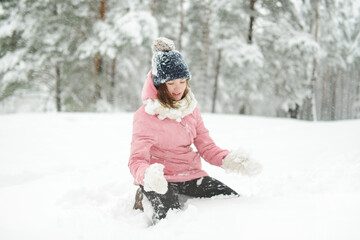 Fototapeta na wymiar Adorable girl having fun in beautiful winter park during snowfall. Cute child playing in a snow. Winter activities for family with kids.