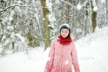 Fototapeta na wymiar Adorable girl having fun in beautiful winter park during snowfall. Cute child playing in a snow. Winter activities for family with kids.