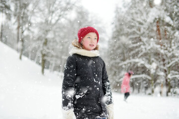 Two young girls having fun together in beautiful winter park. Cute sisters playing in a snow. Winter activities for family with kids.