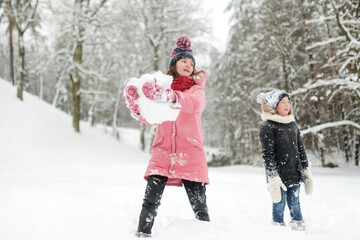 Two young girls having fun together in beautiful winter park. Cute sisters playing in a snow. Winter activities for family with kids.