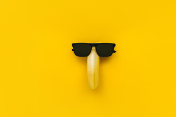 A funny banana with black sunglasses on a yellow paper background. Surveillance, detective,...