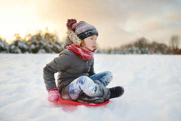 Funny little girl having fun with a sleigh in beautiful winter park. Cute child playing in a snow.