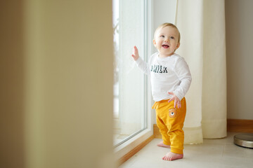 Adorable baby boy standing by the window. Toddler learning how to stand up unassisted.