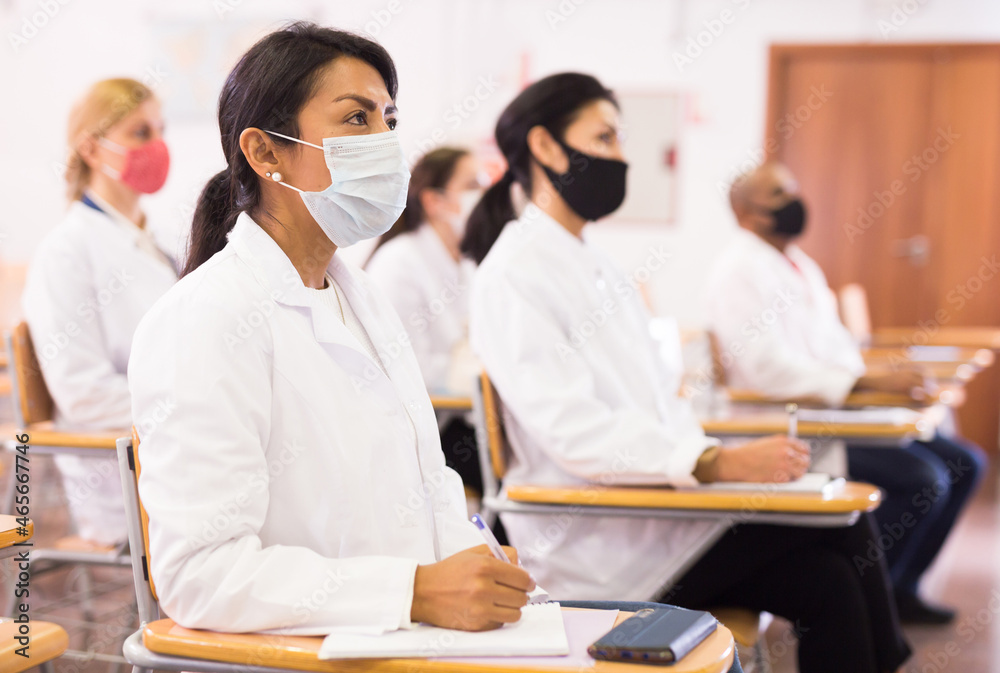 Sticker Portrait of young adult female doctor attentively listening to lecture with colleagues, medical conference during coronavirus pandemic