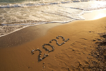 2022 Happy new year concept. Top view of 2022 numbers written on the sand of coastline with wave.Message hand written in golden sand on beautiful sunset or sunrise golden sky background            