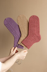 Three woolen socks in women hands on beige background