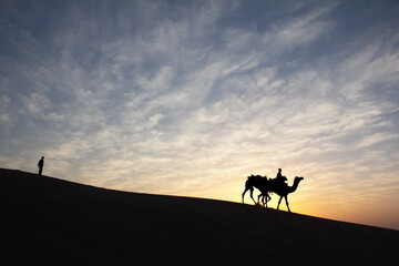 Fototapeta na wymiar Silhouette of man and his camel at colorful sunset