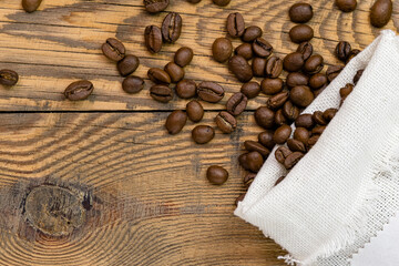 Coffee beans are scattered from a canvas bag on a wooden background. Space for text on a canvas bag, coffee grains on a wooden background.