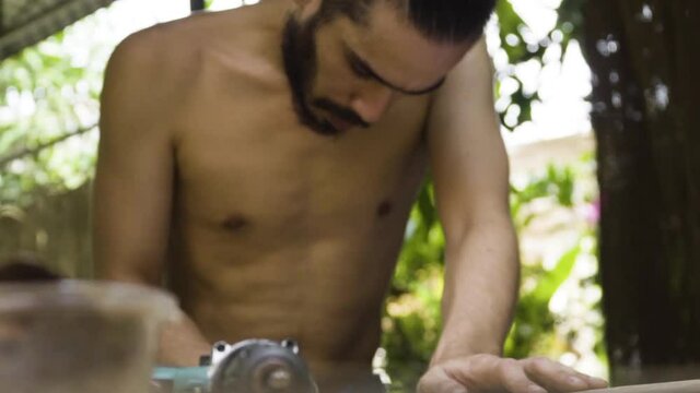 Young male craftsman working on wooden skateboard, handheld view
