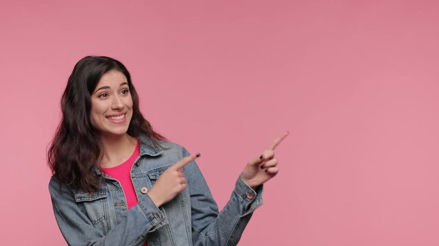 Shocked young woman 20s years old in casual denim jacket pink t-shirt posing look camera pointing fingers hands on copy space workspace isolated on pink background in studio. People lifestyle concept.