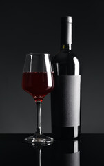 Bottle and glass of red wine on black background