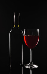 Bottle and glass of red wine on black background