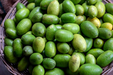 Many lemons are put in a bamboo basket and their color is green and background blur