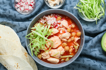 Bowl with delicious pozole soup and ingredients on table