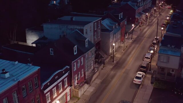 Aerial of quiet urban city street at night. lights and row homes. American USA establishing shot.