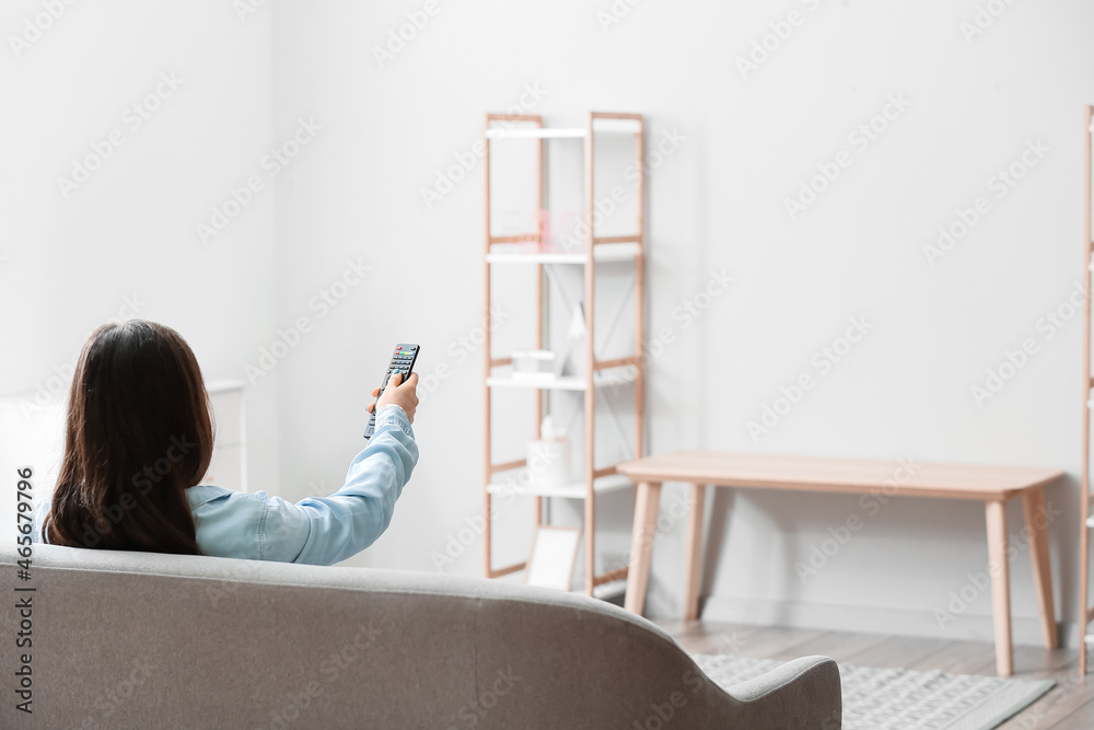 Poster woman with tv remote control sitting on sofa at home